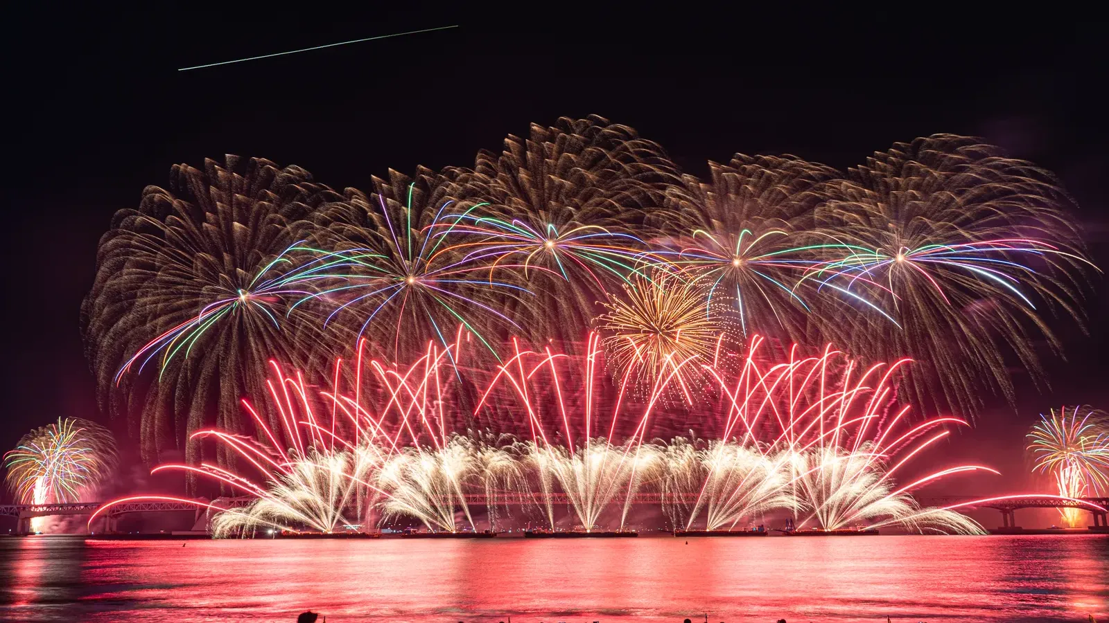 Fireworks bursting over Gwangan Bridge as crowds watch from the beach