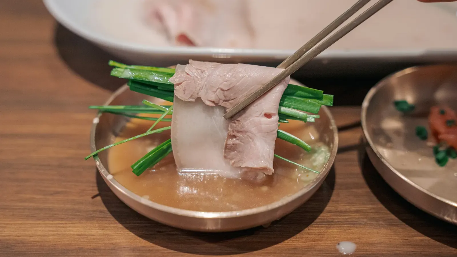 Slices of boiled pork with chives in broth, lifted with chopsticks