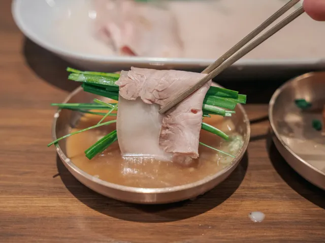 Slices of boiled pork with chives in broth, lifted with chopsticks