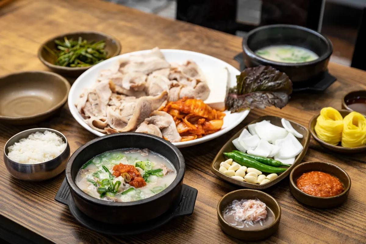 A dwaeji-gukbap set with a stone bowl of pork bone soup, sliced boiled pork, and kimchi
