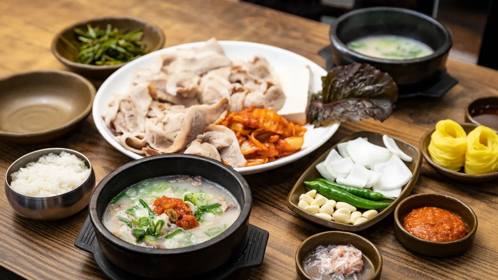 A dwaeji-gukbap set with a stone bowl of pork bone soup, sliced boiled pork, and kimchi