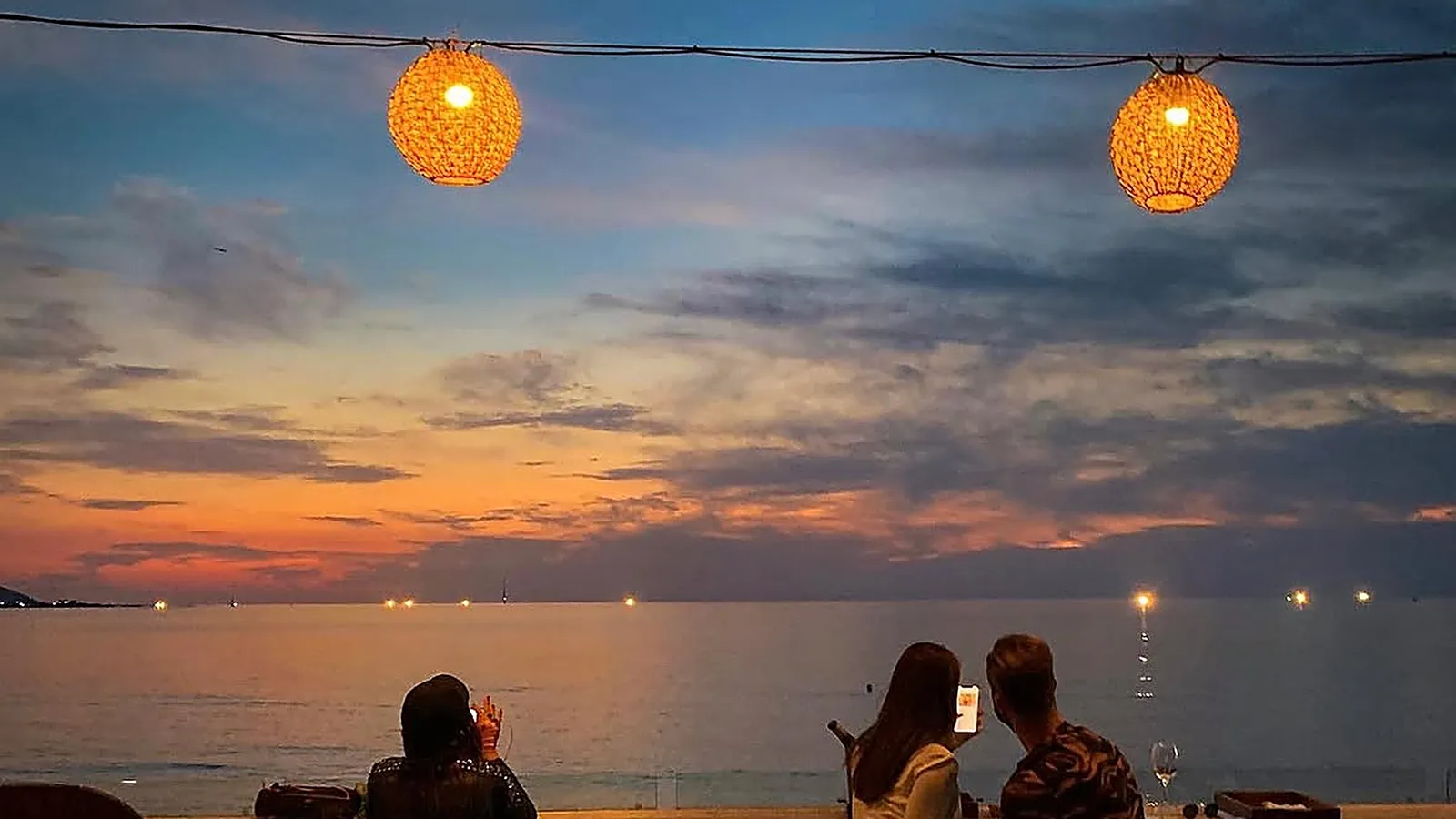 海辺のルーフトップ席から夕焼け雲を眺める旅行者