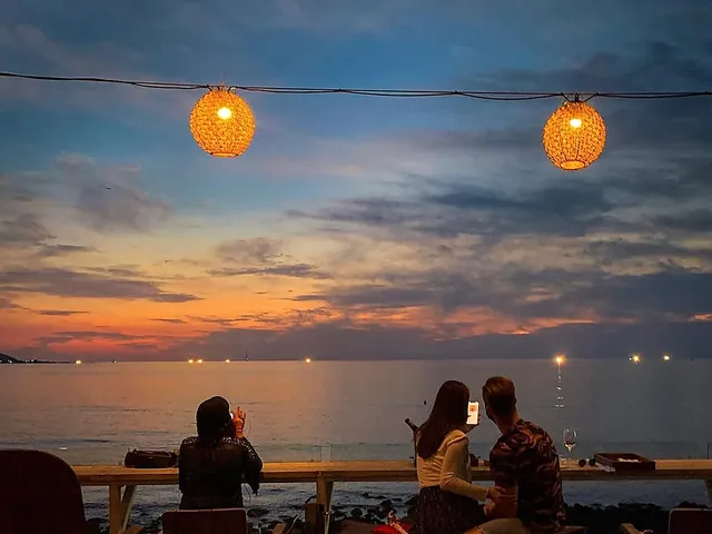 海辺のルーフトップ席から夕焼け雲を眺める旅行者