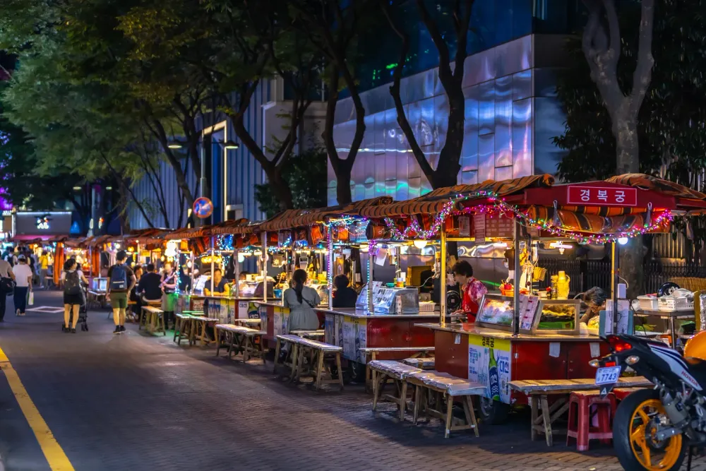A row of lit-up food cart stalls with seating along a Seomyeon street at night